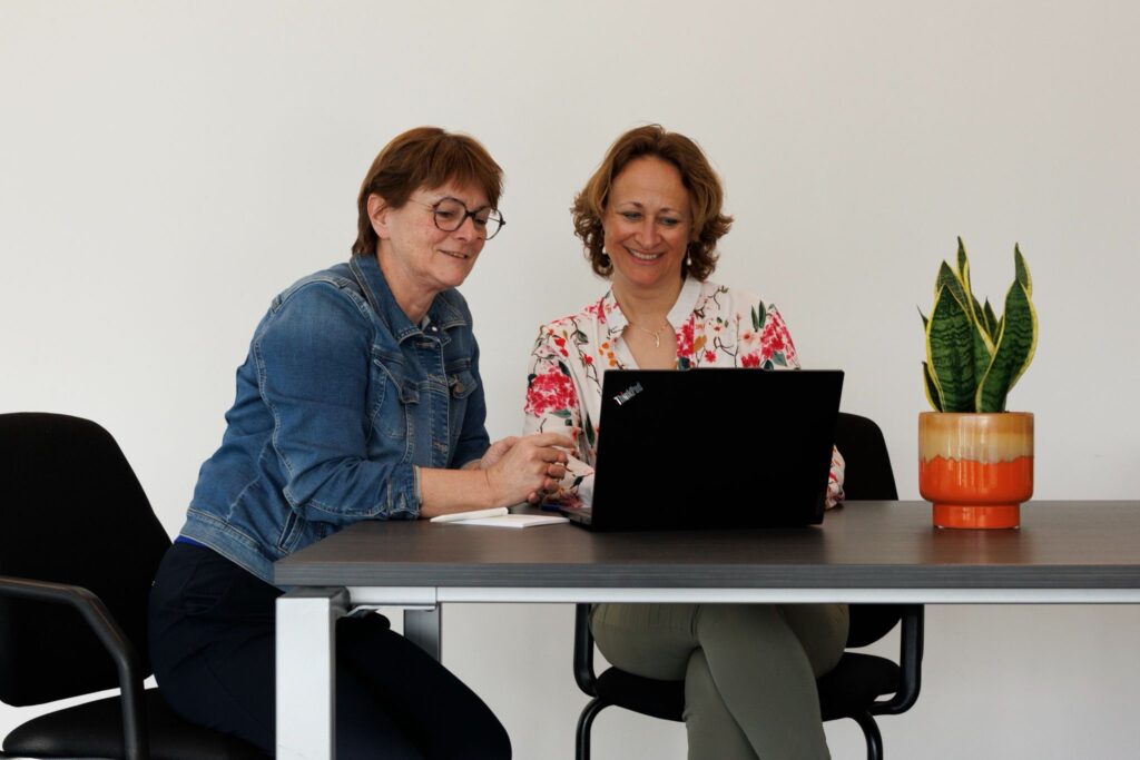 Collega's zitten aan tafel en kijken samen naar laptop